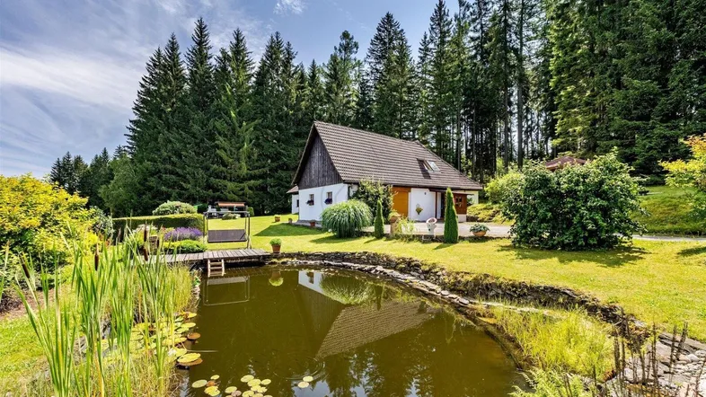 Idyllisches Landhaus umgeben von einem gepflegten Garten mit Teich und Wald im Hintergrund.