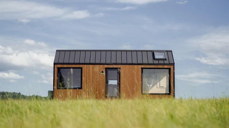 Modernes Tiny House mit Holzfassade und dunklem Metalldach in einer weiten Wiese.