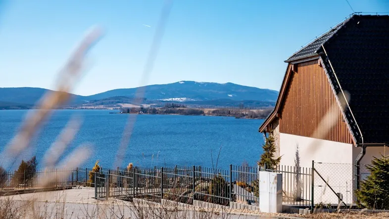Haus mit Blick auf den See und die umliegenden Berge unter blauem Himmel.