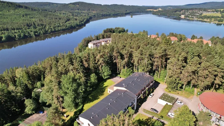 Luftaufnahme der Wohngebäude in waldreicher Umgebung mit weitem Blick auf den See.