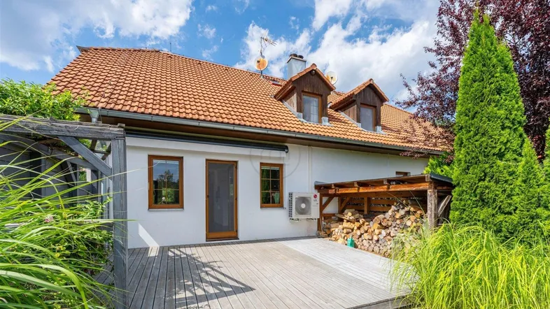 Große Holzterrasse am Haus mit Blick ins Grüne und Brennholzlager unter einem Unterstand.