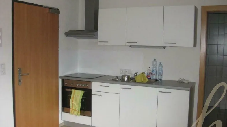 Kleine Einbauküche mit weißen Schränken, integriertem Backofen und Dunstabzugshaube.