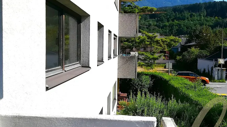 Blick vom Balkon auf die umliegende Berglandschaft und die benachbarten Gebäude.