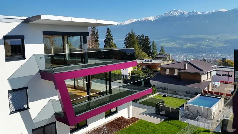 Moderne Architektur mit großen Glasfronten, Balkonen und Bergblick in sonniger Lage.