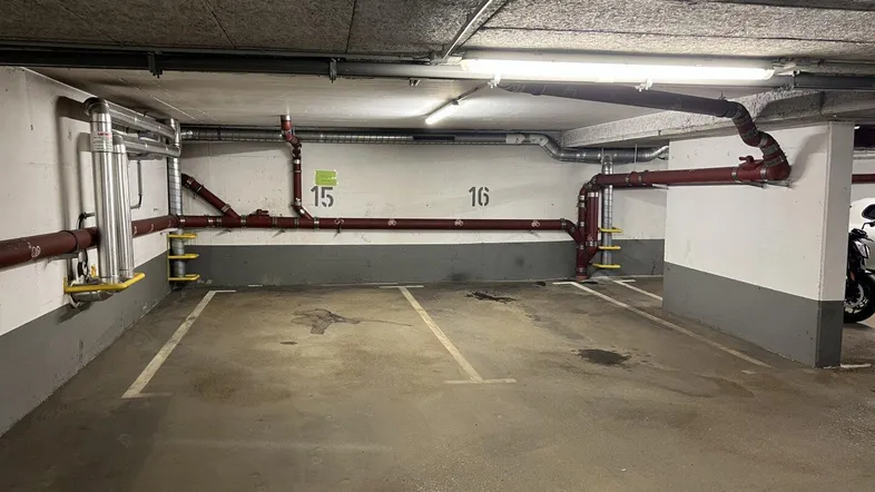 Tiefgarage mit markierten Parkplätzen und sichtbaren Versorgungsleitungen an der Decke.