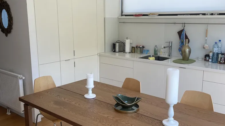 Helle, moderne Küche mit weißen Schränken, Holztisch und offenem Essbereich.