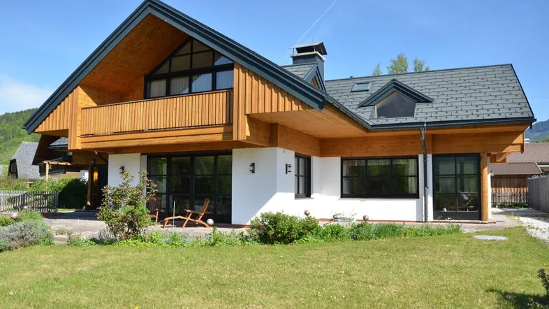 Attraktives Einfamilienhaus mit Holzfassade, weißem Putz und gepflegtem Garten vor Bergkulisse.