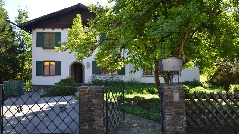 Traditionelles Haus mit weißer Fassade, grünen Fensterläden und schmiedeeisernem Tor.