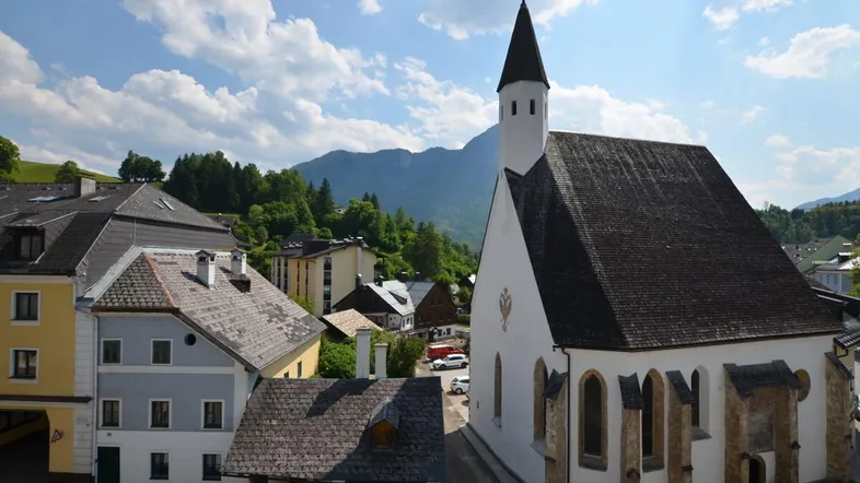 Malerische Ansicht eines Dorfes mit Kirche und Bergen unter blauem Himmel.