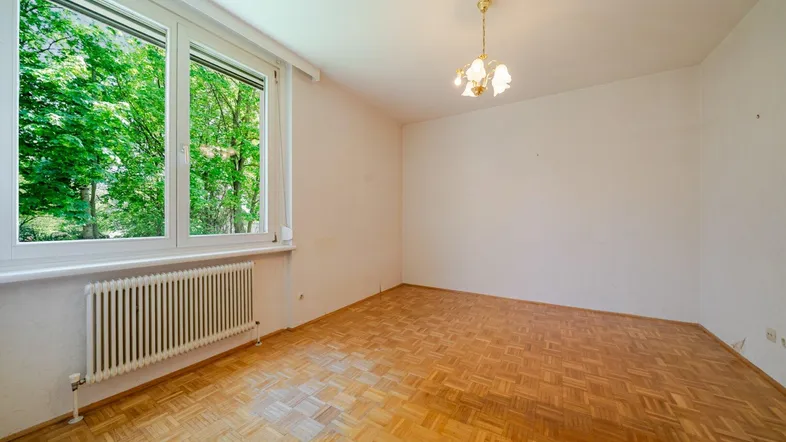 Heller Raum mit Parkettboden und großem Fenster, das viel Tageslicht hereinlässt.