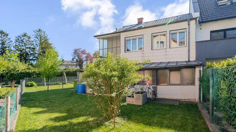 Gepflegter Gartenbereich mit Rasenfläche, Sträuchern und Blick auf die Rückseite des Hauses.