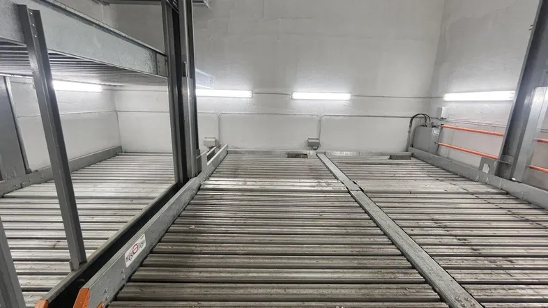 Nahaufnahme des Stapelparksystems in einer Tiefgarage mit Metallplattformen und orangefarbenen Sicherheitsgeländern.
