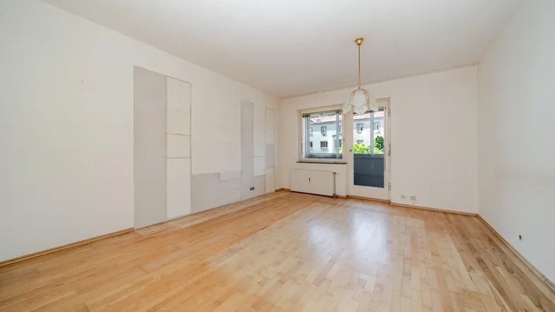 Helles, leeres Zimmer mit hellem Parkettboden, weißen Wänden und Zugang zu einem kleinen Balkon.