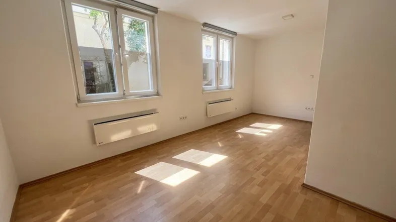 Helles Zimmer mit Parkettboden, weißen Wänden und Blick ins Grüne durch die Fenster.