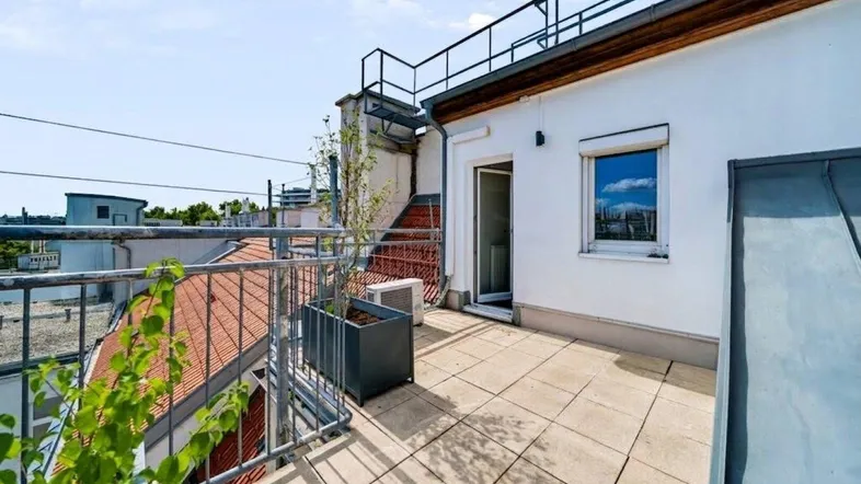Geräumige Dachterrasse mit Fliesenboden, Metallgeländer und Blick auf die umliegenden Gebäude.