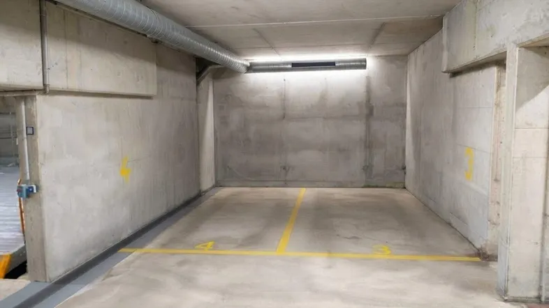 Leerer Stellplatz in einer Tiefgarage mit Betonwänden und Decke sowie sichtbaren Lüftungsrohren.