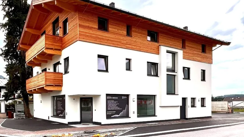 Modernes Gebäude mit weißer Fassade und Holzverkleidung, ausgestattet mit Balkonen und großen Fenstern.