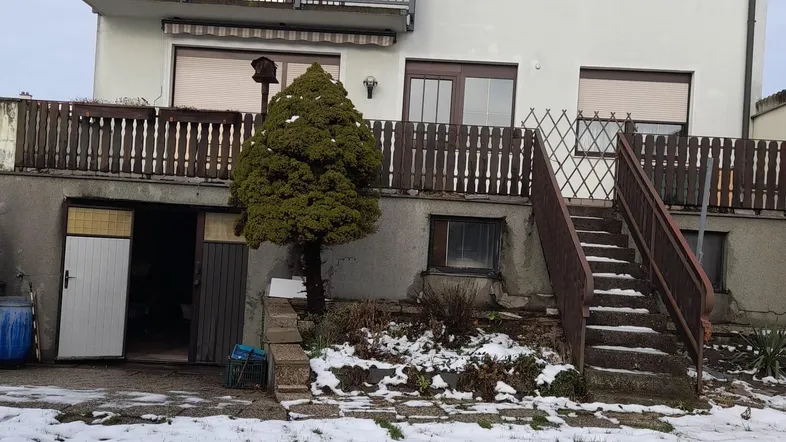 Mehrfamilienhaus mit Balkon und Außentreppe, umgeben von Schnee im Winter.