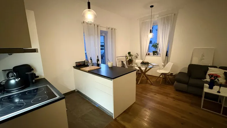 Offener Wohn- und Essbereich mit moderner Kücheninsel, Holzboden und gemütlicher Sitzecke.