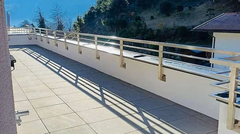 Geräumige Dachterrasse mit Fliesenboden, modernem Geländer und weitem Blick auf die umliegenden Berge.
