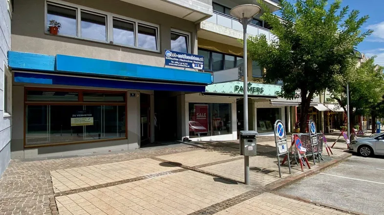 Fassade eines Geschäftsgebäudes mit Schaufenstern und Bürgersteig in einer städtischen Umgebung.