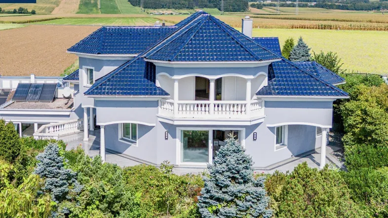 Elegante Fassade des Hauses mit blauen Dächern, Balkonen und gepflegter Bepflanzung.