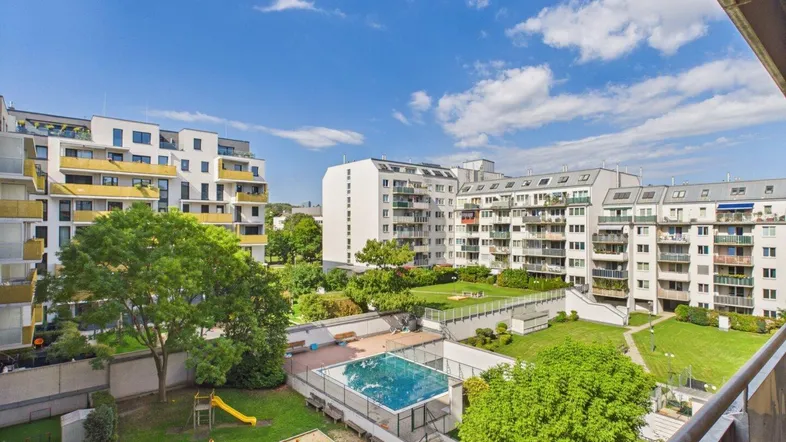 Blick vom Balkon auf die gepflegte Wohnanlage mit Gemeinschaftspool, Spielplatz und Grünflächen.
