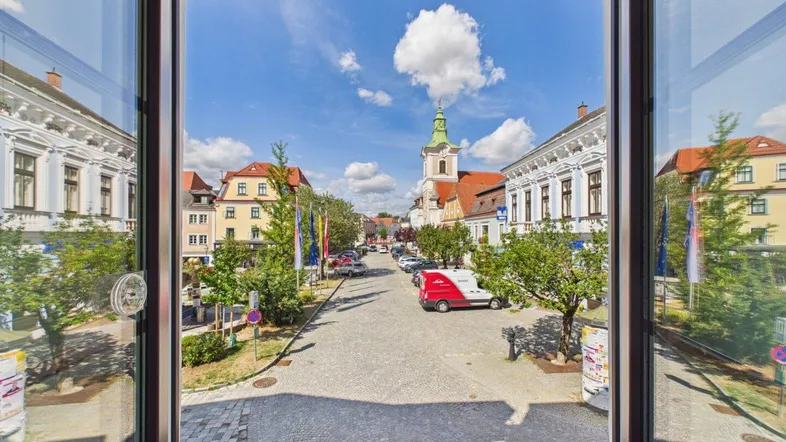 Blick aus einem Fenster auf eine belebte Kopfsteinpflasterstraße mit historischen Gebäuden und einem Kirchturm.