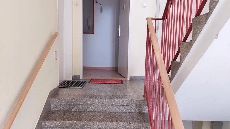 Treppenhaus mit Granitstufen und rotem Geländer, führt zu den Wohneinheiten.