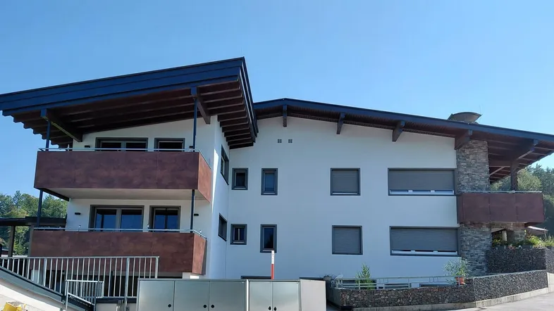 Modernes Mehrfamilienhaus mit Balkonen und traditionellem Satteldach in sonniger Lage.