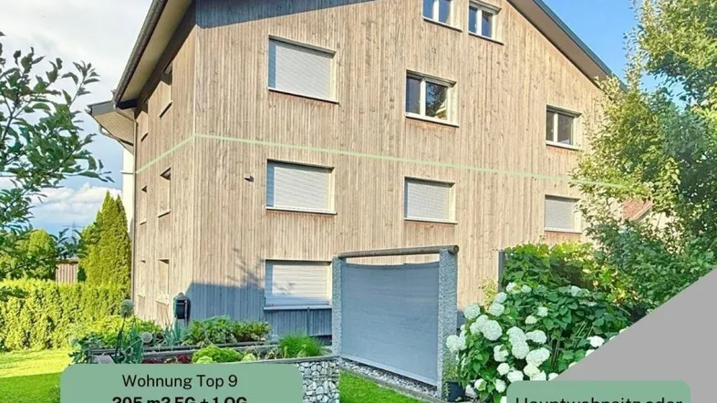 Modernes Mehrfamilienhaus mit Holzfassade und gepflegtem Gartenbereich, umgeben von grüner Natur.