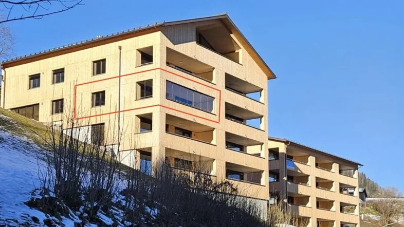 Modernes Mehrfamilienhaus in Holzbauweise am Hang mit Balkonen und verschneiter Umgebung.