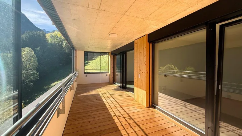 Geräumiger Holzbalkon mit Glasbrüstung und weitem Blick auf die umliegende Berglandschaft.