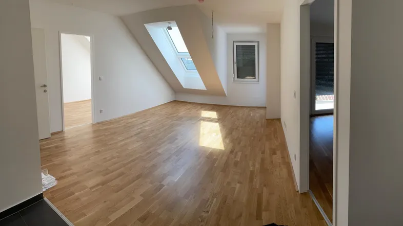 Helles Wohnzimmer mit Dachschrägen, Parkettboden und Dachfenstern, bereit zur Einrichtung.