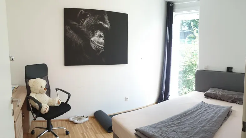 Helles Schlafzimmer mit Holzboden, großem Fenster und einem Schreibtischbereich.