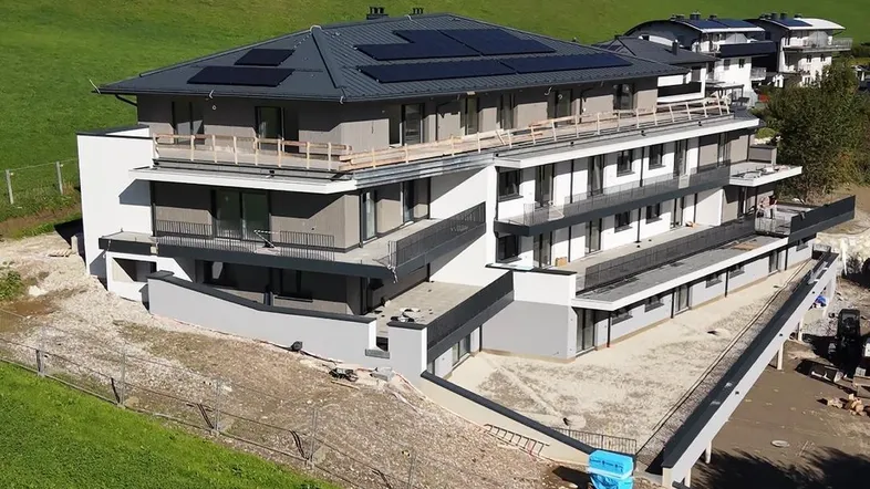 Modernes Mehrfamilienhaus in Hanglage mit Solaranlage und Bergblick.