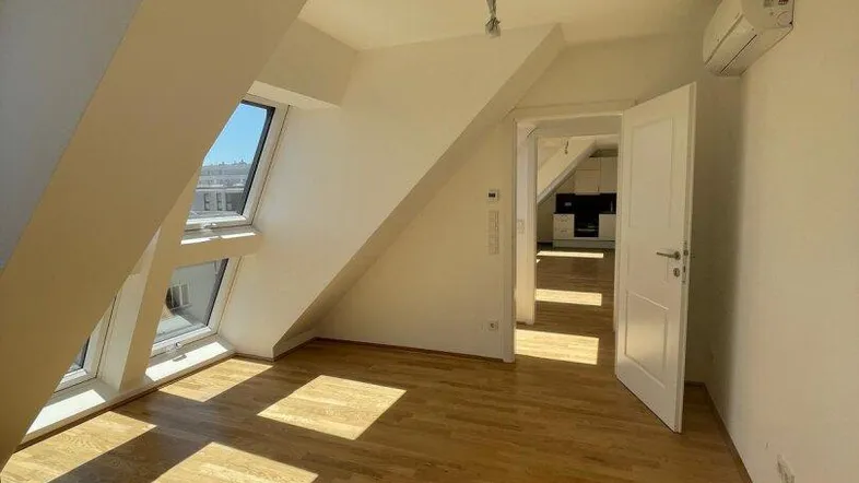 Helles Dachgeschosszimmer mit Holzboden, schrägen Wänden und großen Dachfenstern, die viel Sonnenlicht hereinlassen.