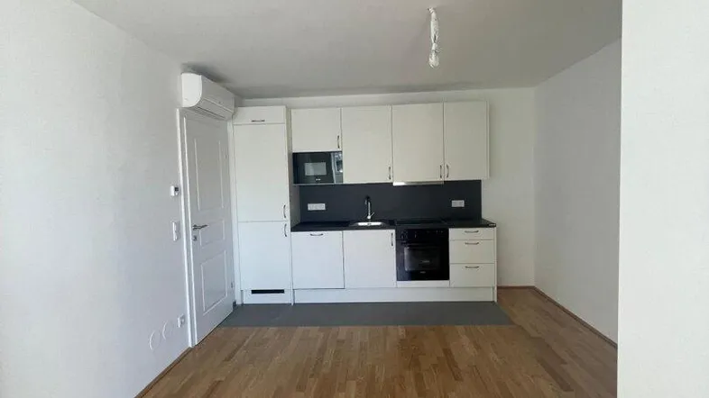 Helle Küche mit weißen Schränken, dunkler Arbeitsplatte und Holzboden in einem offenen Wohnbereich.