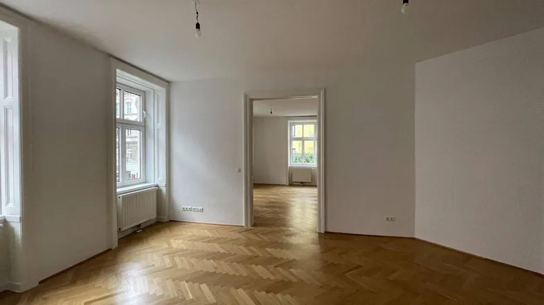 Helles, leeres Zimmer mit Fischgrätparkett und hohen Fenstern, bereit zur individuellen Gestaltung.