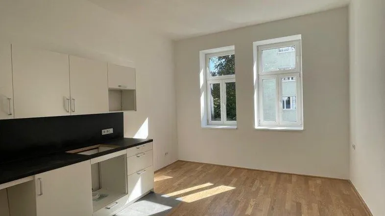 Heller Küchenbereich mit weißen Einbauschränken, Holzboden und viel Tageslicht durch die Fenster.