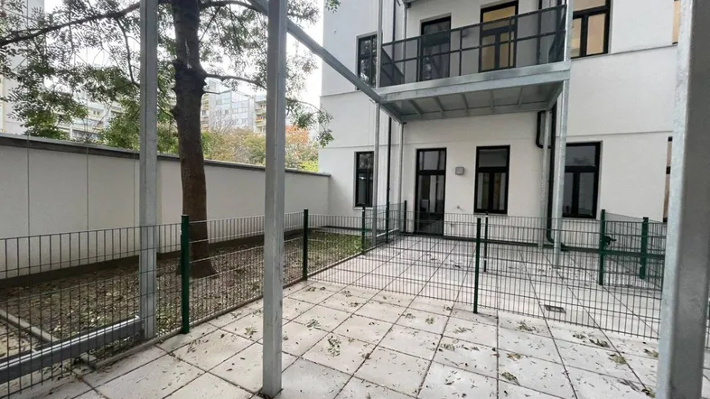 Gepflasterte Terrasse im Erdgeschoss mit Zugang zu einem kleinen Gartenbereich und Blick auf die Gebäudefassade.