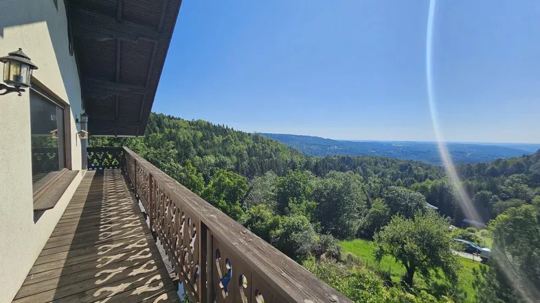 Langer Holzbalkon mit traditionellem Geländer und weitem Blick über bewaldete Hügel und das Tal.