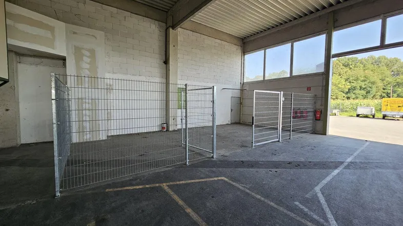 Große Lagerhalle mit Betonboden, hohen Decken und Gitterabtrennungen, die verschiedene Bereiche abgrenzen.
