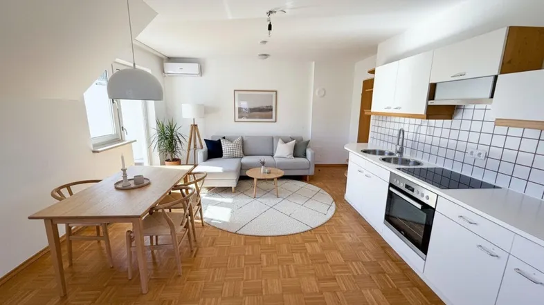 Helles, offenes Wohn-Esszimmer mit integrierter Küche, Parkettboden und moderner Einrichtung.