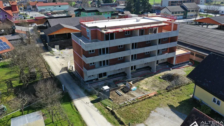 Luftaufnahme eines im Bau befindlichen Mehrfamilienhauses mit Rohbau und umliegender Bebauung.