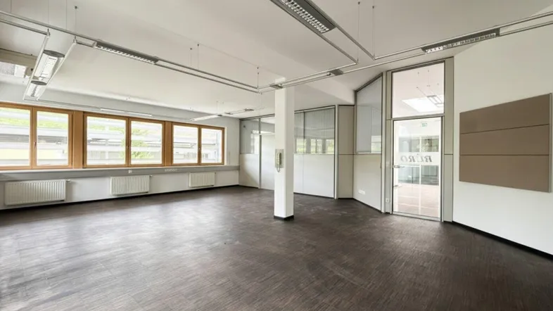 Geräumiges Büro mit großen Fenstern, dunklem Boden und heller Decke, ideal für flexible Arbeitsbereiche.