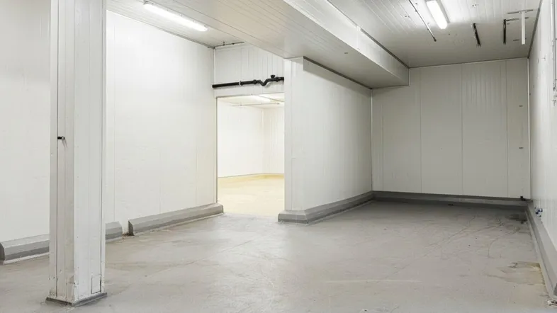 Großer, leerer Lagerraum mit weißen Wänden, Betonboden und sichtbaren Säulen, bereit zur Nutzung.