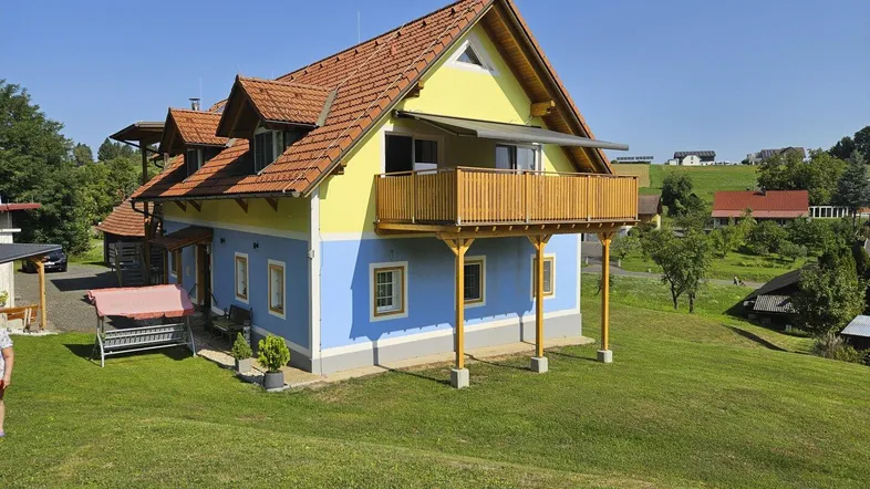 Traditionelles Haus mit gelb-blauer Fassade, Holzbalkon und Satteldach in ländlicher Umgebung.