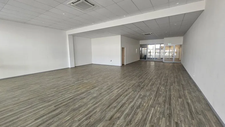 Geräumiger, leerer Gewerberaum mit modernem Laminatboden und abgehängter Decke, bereit für den Erstbezug.