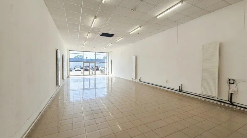 Großzügiger, leerer Gewerberaum mit Fliesenboden und großen Schaufenstern zur Straße.